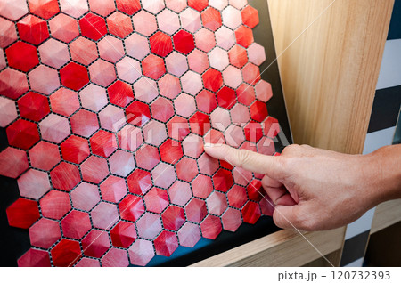 Designer hand pointing at red hexagon pattern mosaic tile on ceramic collection display shelf 120732393