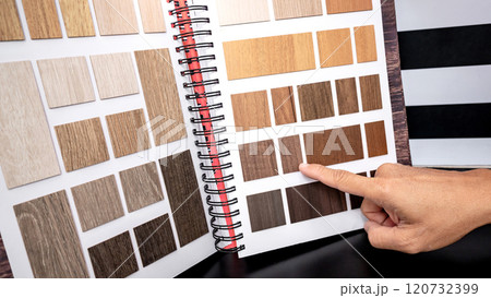 Designer hand pointing at wooden laminate swatch collection in material sample catalog Designer hand pointing at wooden laminate swatch collection in material sample catalog 120732399