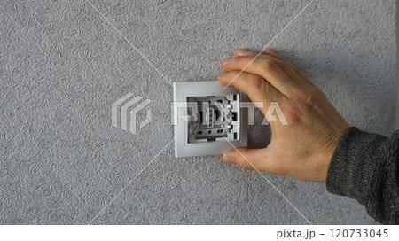 male hand applying white plastic switch housing to base in wall with gray wallpaper, DIY home electrical switch installation 120733045