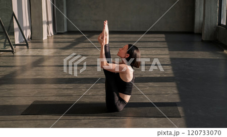 Yoga training. Strength exercise. Athletic sport woman in activewear doing leg lift body stretch workout holding feet on mat in fitness studio with free space. Yoga training. Strength exercise. Athletic sport woman in activewear doing leg lift body stretch workout holding feet on mat in fitness studio with free space. 120733070