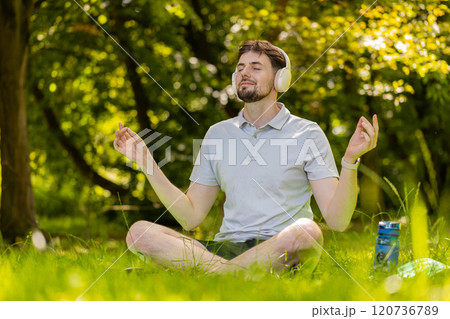 Young man sitting on mat in lotus position, relaxing in city park on summer day meditation relax 120736789