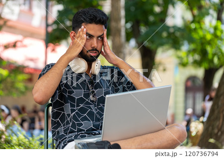 Hispanic sad young man using laptop receive bad email message news, game fail in urban city street Hispanic sad young man using laptop receive bad email message news, game fail in urban city street 120736794