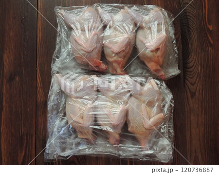 skinned domestic quail carcasses wrapped in three plastic bags placed on a textured dark stained wood countertop, farm-raised featherless poultry in clear packaging material skinned domestic quail carcasses wrapped in three plastic bags placed on a textured dark stained wood countertop, farm-raised featherless poultry in clear packaging material 120736887