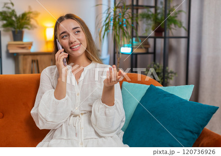 Happy young Caucasian woman making mobile phone conversation with friends sitting on couch at home 120736926