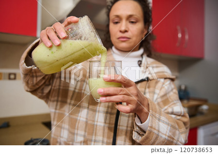 Woman pouring fresh green smoothie in modern kitchen setting Woman pouring fresh green smoothie in modern kitchen setting 120738653