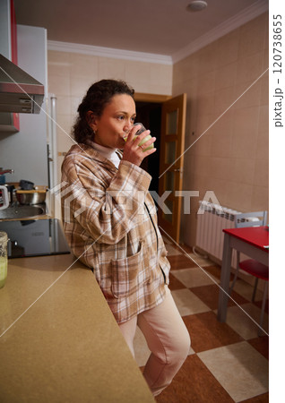 Woman enjoying a healthy green smoothie in her kitchen 120738655