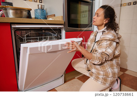 Woman kneeling in kitchen loading dishwasher with dishes Woman kneeling in kitchen loading dishwasher with dishes 120738661
