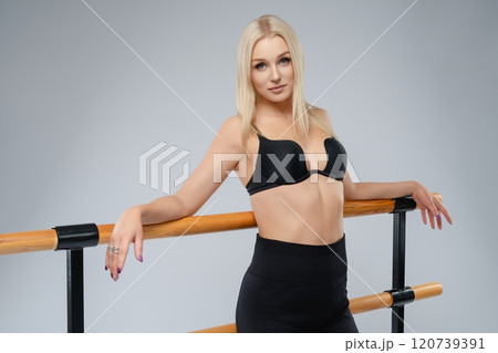 Young woman posing confidently at a ballet barre in a studio setting 120739391
