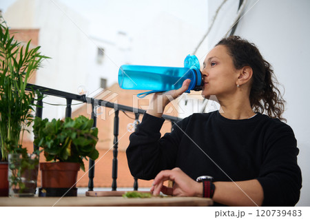Woman drinking water on balcony with plants around Woman drinking water on balcony with plants around 120739483