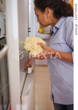 Woman holding cauliflower while looking inside the refrigerator Woman holding cauliflower while looking inside the refrigerator 120739508
