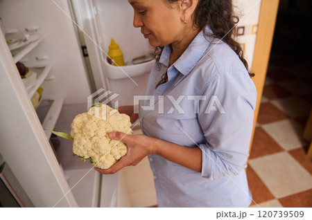 Woman holding fresh cauliflower in front of an open refrigerator 120739509