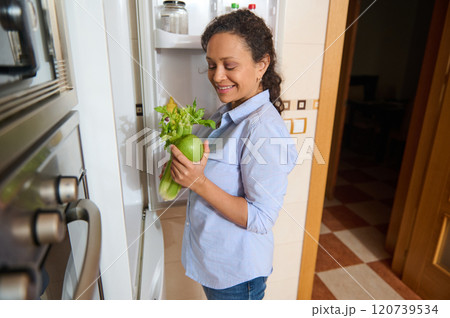 Woman happily holding fresh vegetables in her home kitchen 120739534
