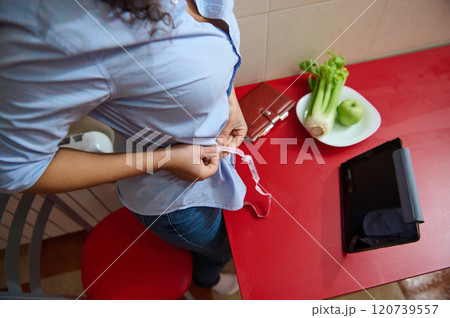 Woman measuring waist with tape near healthy food and tablet Woman measuring waist with tape near healthy food and tablet 120739557