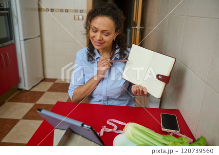 Woman video conferencing in kitchen with notebook and tablet 120739560