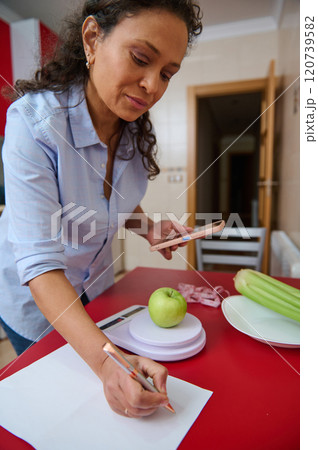 Woman tracking apple calorie intake with smartphone at home 120739582