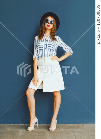Fashion lady woman wearing a black sunglasses, hat and white skirt posing over a gray background Fashion lady woman wearing a black sunglasses, hat and white skirt posing over a gray background 120739635