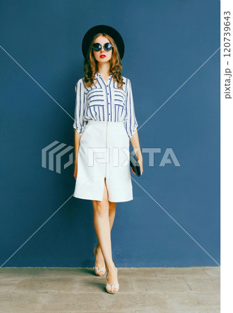Fashion woman in black round hat, white skirt and handbag clutch posing over a gray background Fashion woman in black round hat, white skirt and handbag clutch posing over a gray background 120739643