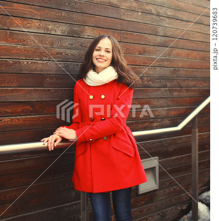 Beautiful young smiling woman wearing a red coat and scarf in city Beautiful young smiling woman wearing a red coat and scarf in city 120739683