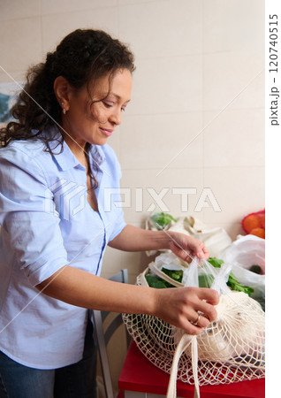 Woman unpacking organic vegetables from reusable bag in kitchen Woman unpacking organic vegetables from reusable bag in kitchen 120740515