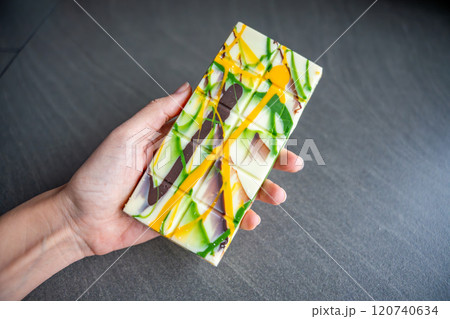 Trend Dubai white chocolate with pistachio paste and kataifi dough in woman hand. Confectionery handmade sweets at home in the kitchen. Trend Dubai white chocolate with pistachio paste and kataifi dough in woman hand. Confectionery handmade sweets at home in the kitchen. 120740634