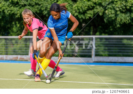 Two young female athletes compete in intense field hockey match during sunny day 120740661