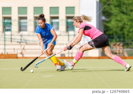 Two young female athletes compete in intense field hockey match during sunny day 120740665
