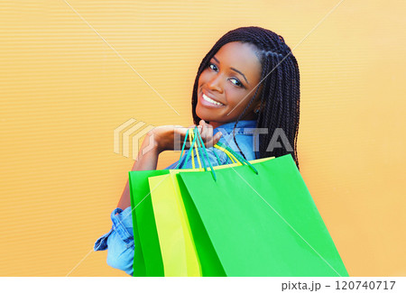 Fashion happy smiling african woman with shopping bags in city over colorful orange background Fashion happy smiling african woman with shopping bags in city over colorful orange background 120740717