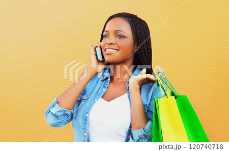 Fashion happy smiling african woman with shopping bags talking on phone on orange background Fashion happy smiling african woman with shopping bags talking on phone on orange background 120740718