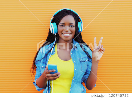 Fashion pretty smiling african woman in headphones listens to music over orange background Fashion pretty smiling african woman in headphones listens to music over orange background 120740732