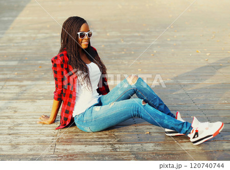 Fashion young african woman sitting in a city park, wearing a red checkered shirt and sunglasses Fashion young african woman sitting in a city park, wearing a red checkered shirt and sunglasses 120740744