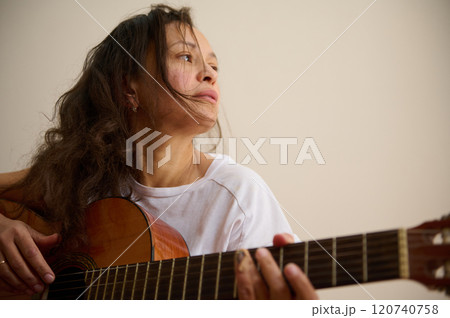 Woman in white shirt playing acoustic guitar thoughtfully indoors 120740758