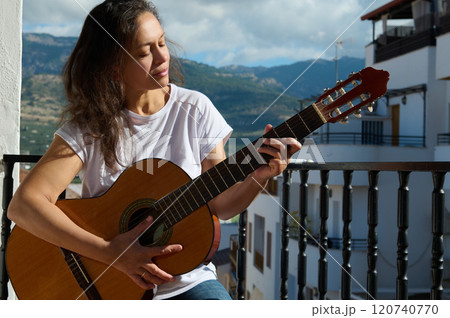 Woman playing guitar on sunny balcony with mountain backdrop Woman playing guitar on sunny balcony with mountain backdrop 120740770