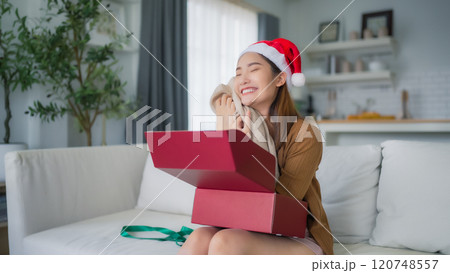 Young Asian woman wearing Christmas hat and opening a gift box Young Asian woman wearing Christmas hat and opening a gift box 120748557
