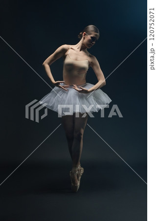 Graceful ballet dancer performing en pointe in a dark studio setting Graceful ballet dancer performing en pointe in a dark studio setting 120752071