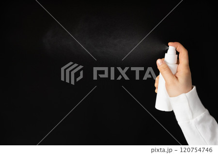 Spray in hand, black background. Spraying the product from a plastic bottle Spray in hand, black background. Spraying the product from a plastic bottle 120754746