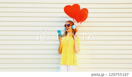 Happy smiling young woman with phone, red heart balloons listening to music in headphones on white Happy smiling young woman with phone, red heart balloons listening to music in headphones on white 120755187
