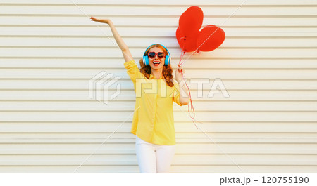 Happy smiling young woman listening to music in headphones holding red heart balloons on white Happy smiling young woman listening to music in headphones holding red heart balloons on white 120755190