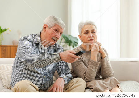 Happy old family at home. Senior couple husband wife watching TV relaxing on sofa in living room. Old mature family enjoying weekend together. Grandparents watching television. Leisure activities 120756348