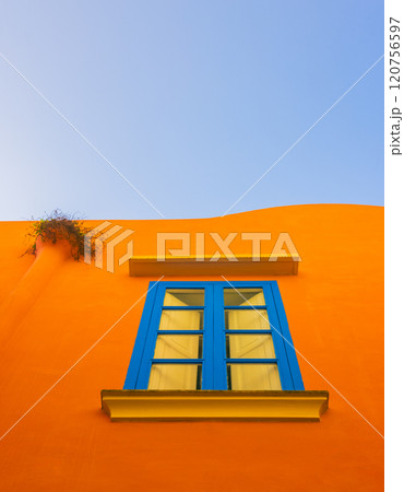 A Stunning and Vibrant Orange Wall Featuring a Blue Window Set Against a Clear Blue Sky in a Capri island A Stunning and Vibrant Orange Wall Featuring a Blue Window Set Against a Clear Blue Sky in a Capri island 120756597