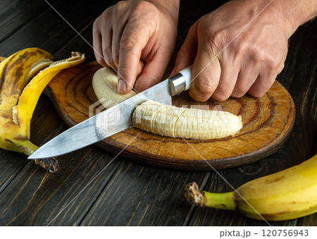 Bright kitchen showcases a person slicing ripe bananas, highlighting culinary artistry. Yellow fruit and a gleaming knife create a vibrant atmosphere for cooking creations 120756943