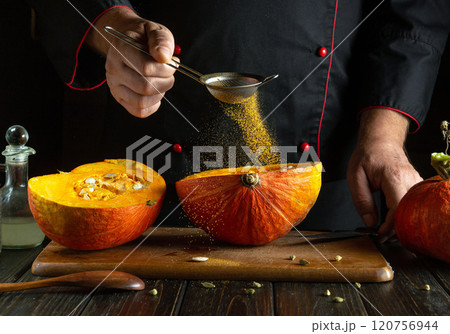 A skilled chef expertly sifts spices onto fresh pumpkin halves in a dimly lit kitchen. The warmth of the wood surrounds a culinary adventure, celebrating seasonal flavors and creativity 120756944