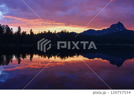 Incredibly beautiful sunset on mountain lake. Trees and a rocky peak reflected 120757554