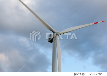 Tall wind turbine under a cloudy sky generating renewable energy in an open field at sunset 120757849