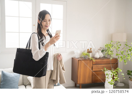 屋内で出かける準備をしてスマホを見る女性 120758574