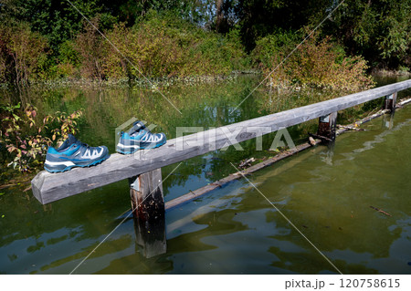 Hiking Shoes On Banister Of Flooded Bridge On Trail At High Water In Danube Wetlands National Park in Austria Hiking Shoes On Banister Of Flooded Bridge On Trail At High Water In Danube Wetlands National Park in Austria 120758615