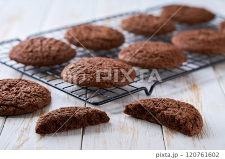 Freshly baked chocolate brownie cookies with cracks cooling on a black wire rack, with in a light kitchen table, selective focus. 120761602