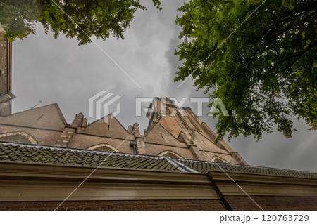 A majestic Gothic church under a dramatic cloudy sky. The intricate brickwork, towering windows, and clock tower reflect its historic architecture and timeless grandeur. 120763729