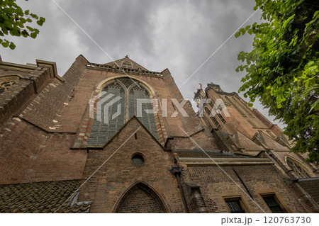 A majestic Gothic church under a dramatic cloudy sky. The intricate brickwork, towering windows, and clock tower reflect its historic architecture and timeless grandeur. 120763730
