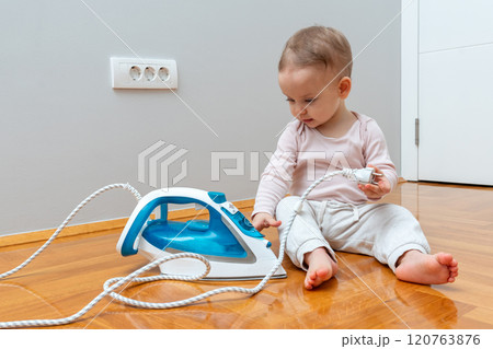 Toddler innocently playing with an iron plug, unaware of potential danger. Toddler innocently playing with an iron plug, unaware of potential danger. 120763876