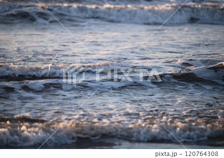 Waves gently lap against shoreline during sunset by ocean Waves gently lap against shoreline during sunset by ocean 120764308
